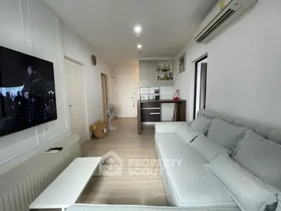 Modern living room with cozy gray sofa and wall-mounted TV, open to a compact kitchen area.