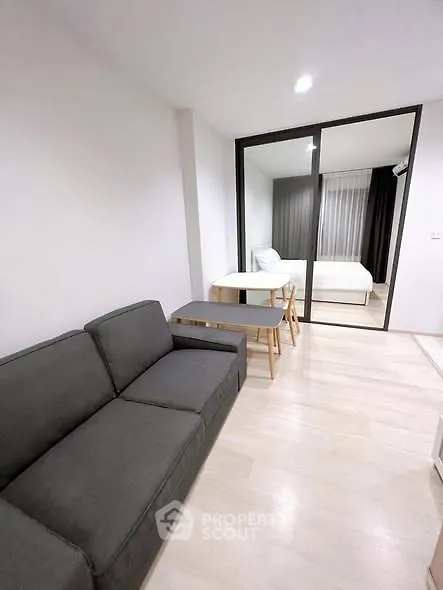 Modern apartment interior with cozy living room and bedroom separated by glass sliding doors.