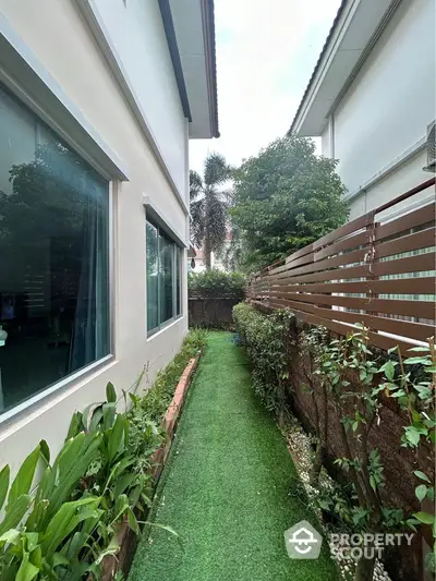 Charming garden pathway beside modern home with lush greenery and privacy fence