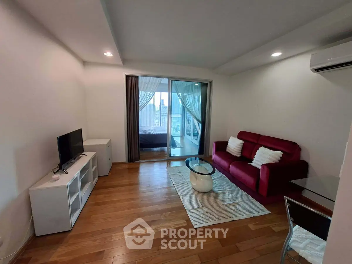 Modern living room with wooden flooring, red sofa, and large window view in a stylish apartment.