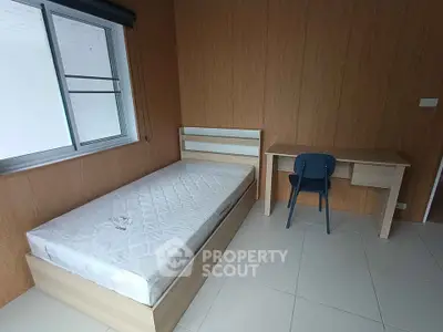 Minimalist bedroom with single bed and study desk, featuring wooden panel walls and large window.