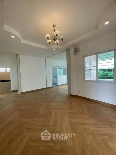 Spacious open-plan living area with elegant chandelier and wooden flooring.