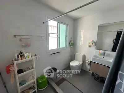 Modern bathroom with window, sink, and toilet in a bright, tiled space.