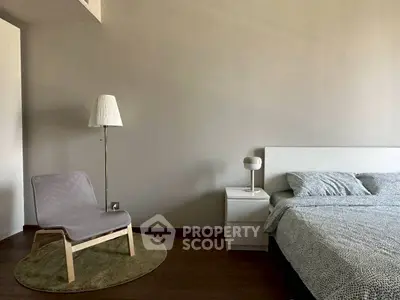 Modern bedroom with stylish chair and lamp, featuring minimalist decor and cozy bedding.