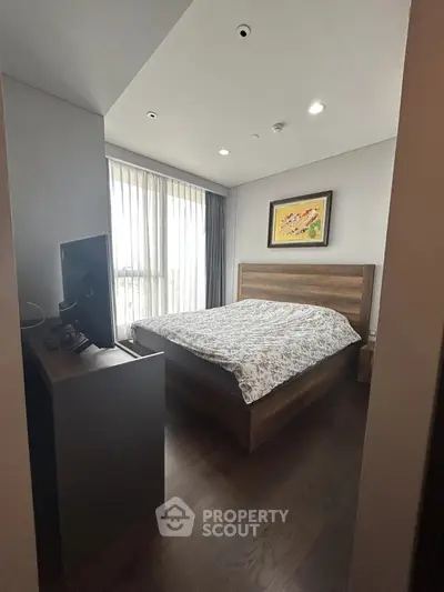 Cozy bedroom with wooden flooring and modern decor, featuring a large window for natural light.