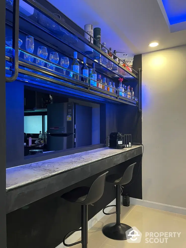 Chic home bar setup with blue accent lighting, modern bar stools, and an array of glassware and bottles on floating shelves.