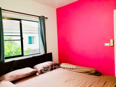Cozy bedroom with vibrant pink accent wall and large window view.