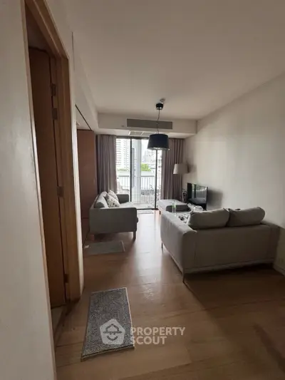 Modern living room with balcony view, cozy seating, and natural light in urban apartment.