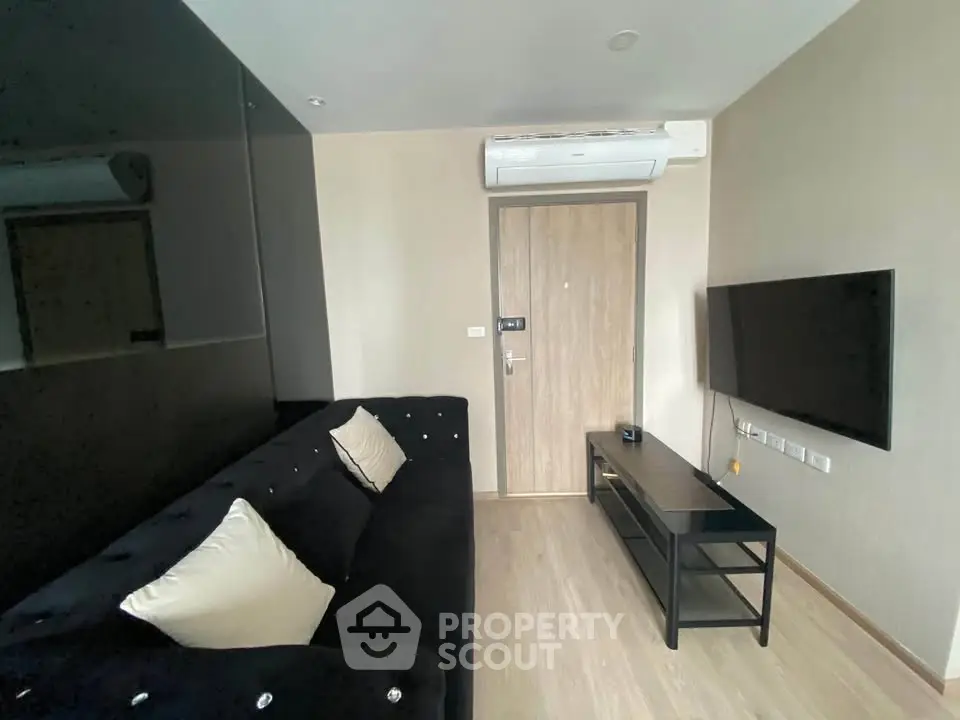 Modern living room with sleek black sofa, wall-mounted TV, and air conditioning unit.