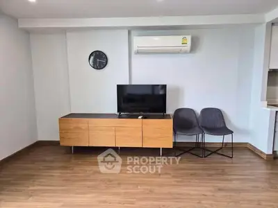 Modern living room with wooden flooring, TV, and air conditioning unit.