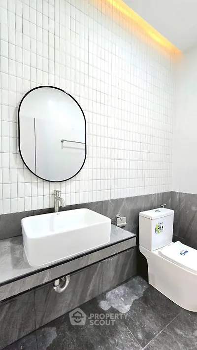 Modern bathroom with sleek design, featuring a stylish oval mirror and contemporary fixtures.