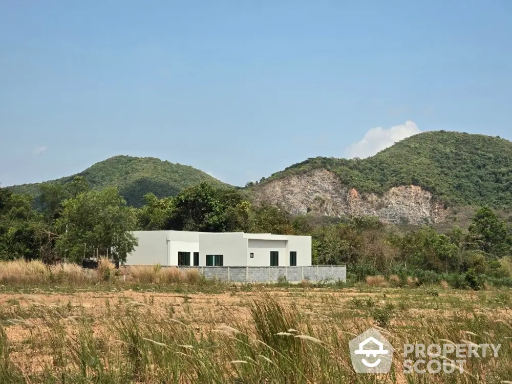 Modern minimalist house with scenic mountain backdrop and expansive open field