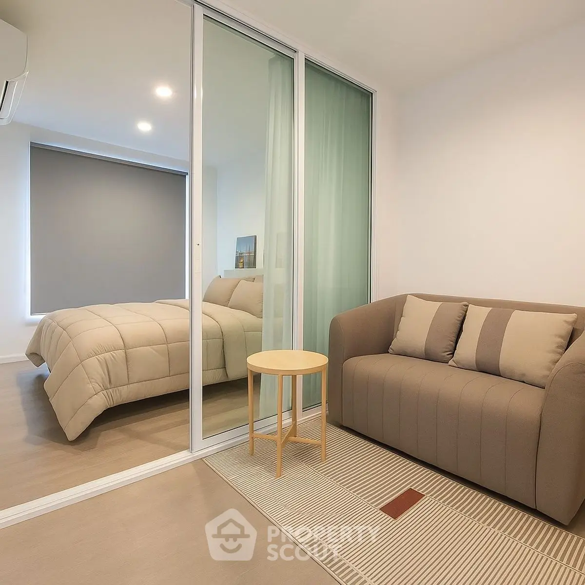 Modern bedroom with cozy sofa and sliding glass partition, featuring minimalist decor and warm lighting.
