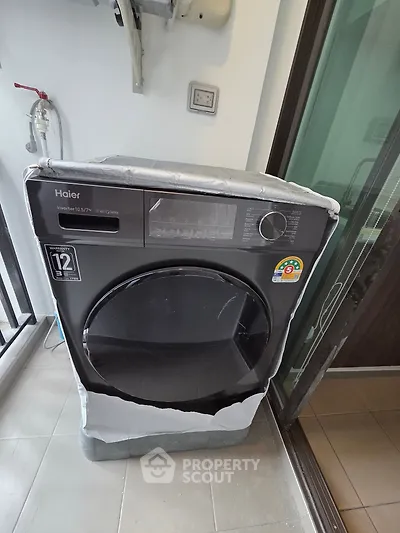 Modern washing machine in a sleek laundry area with glass door and tiled floor.
