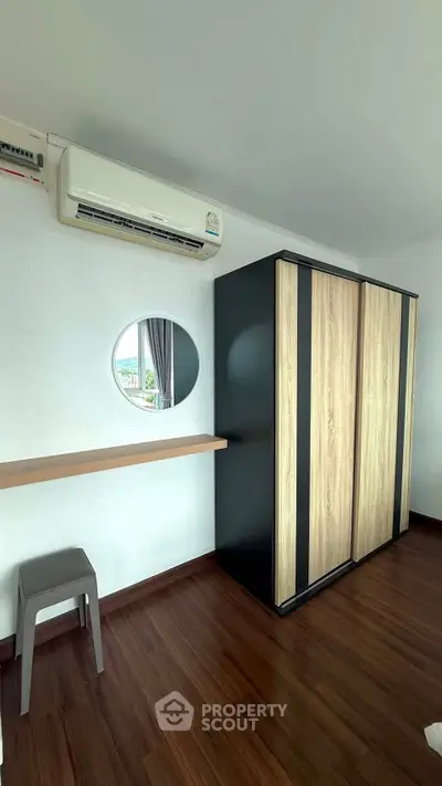 Modern bedroom with sleek wardrobe and air conditioning, featuring a stylish round mirror and wooden flooring.