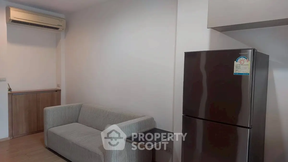 Modern living room with sleek sofa and stainless steel fridge in minimalist design.