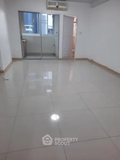 Spacious empty room with glossy tiled flooring and sliding glass doors