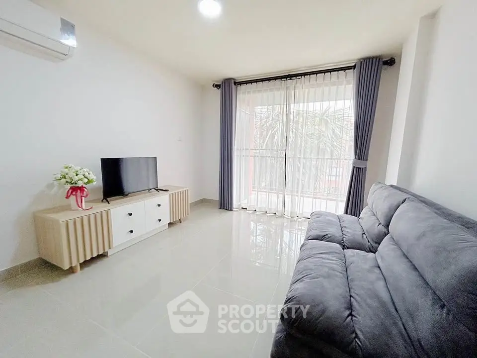Bright and airy living room with modern sofa and TV, featuring large windows and elegant curtains.