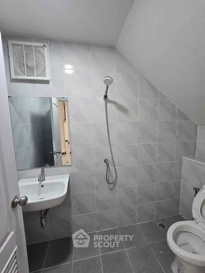 Modern bathroom with sleek tiles and minimalist fixtures, featuring a wall-mounted sink and shower.