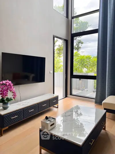 Modern living room with high ceilings and large windows offering natural light and garden view.