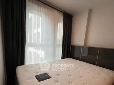 Modern bedroom with large window and elegant curtains, featuring a comfortable mattress.