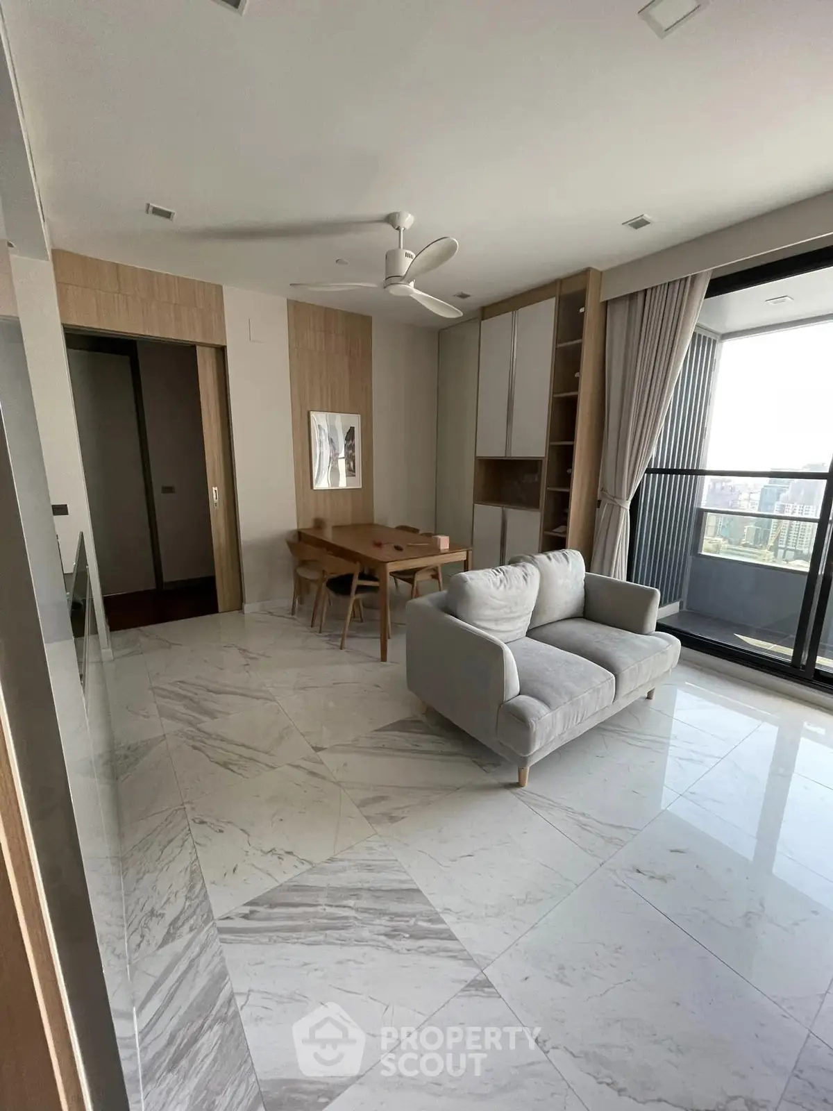 Modern living room with marble flooring, cozy sofa, dining table, and large balcony with city view.