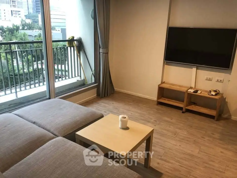 Modern living room with large window and balcony view, featuring a sleek TV setup and cozy seating area.