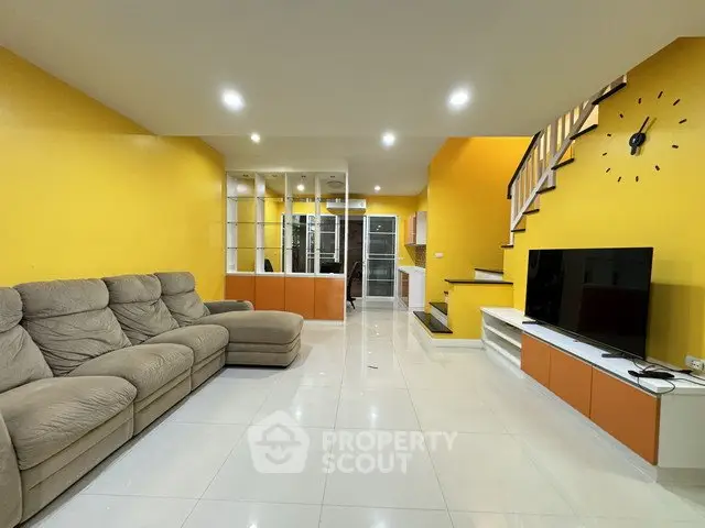 Spacious living room with modern decor and vibrant yellow walls, featuring a cozy sectional sofa and sleek entertainment unit.