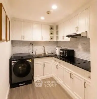 Modern kitchen with sleek cabinetry and appliances, featuring a washing machine and microwave.