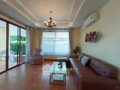Elegant living room with chandelier, leather sofa, and garden view through large windows.