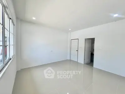 Spacious empty room with glossy tiled floor and large window, perfect for customization.