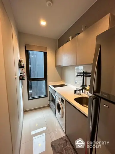 Modern kitchen with sleek cabinets, washing machine, and stainless steel fridge in compact layout.