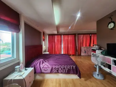 Spacious bedroom with large windows and vibrant red curtains, featuring a comfortable bed and wooden flooring.