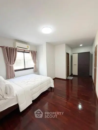 Spacious bedroom with wooden flooring and natural light, featuring a cozy bed and modern wardrobe.