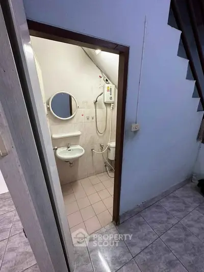 Compact bathroom under staircase with shower and sink in small home