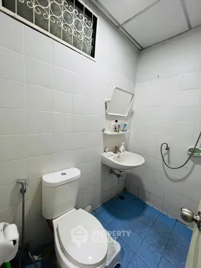 Compact bathroom with white tiles and blue floor, featuring a toilet, sink, and shower area.