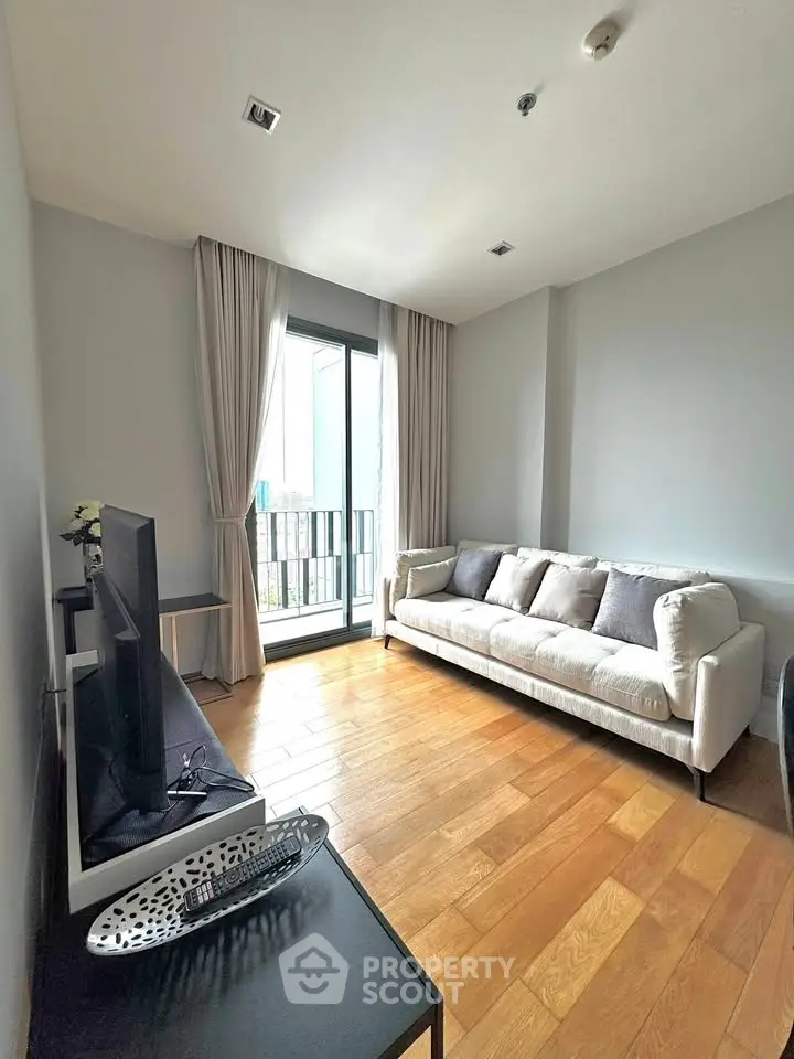 Bright living room with wooden flooring and modern sofa, featuring a large window with city view.