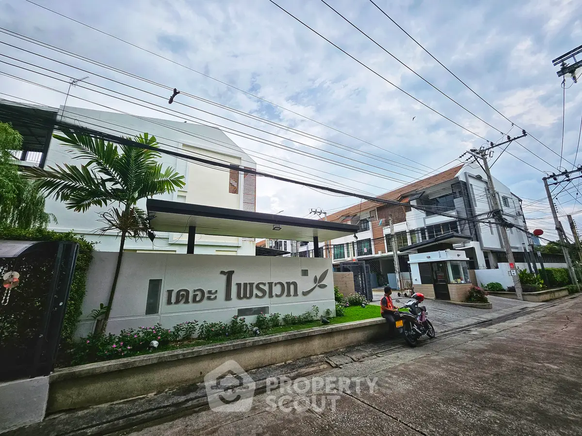 Modern residential building entrance with lush greenery and clear sky, showcasing contemporary urban living.