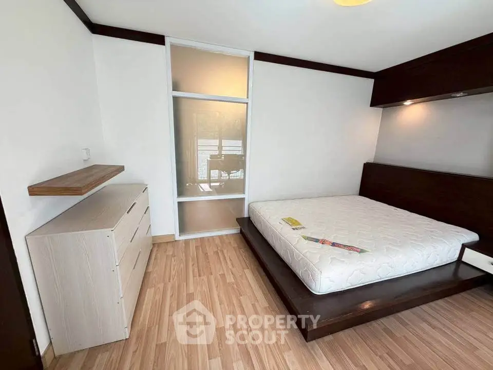 Spacious bedroom with modern design and wooden flooring, featuring a platform bed and ample natural light.