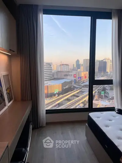 Modern bedroom with city view, featuring large window and sleek furniture.