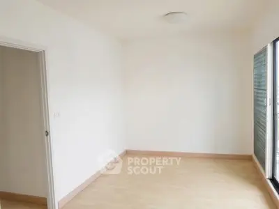 Spacious empty room with wooden flooring and large window, perfect for customization.