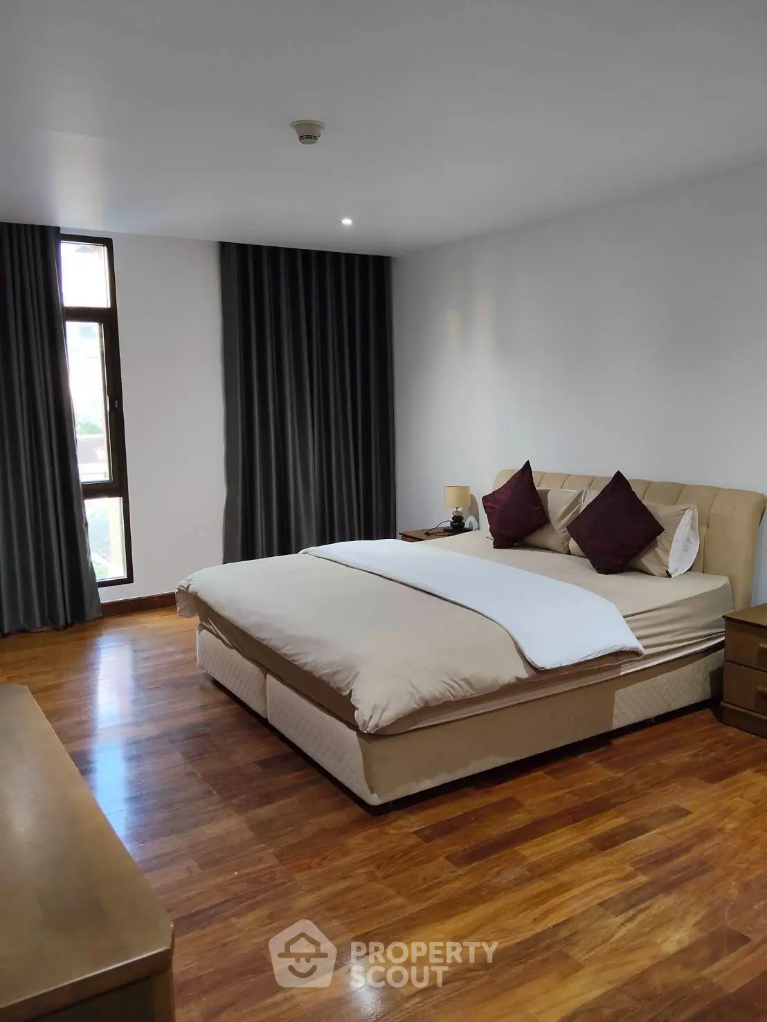 Spacious bedroom with elegant wooden flooring and large window for natural light.