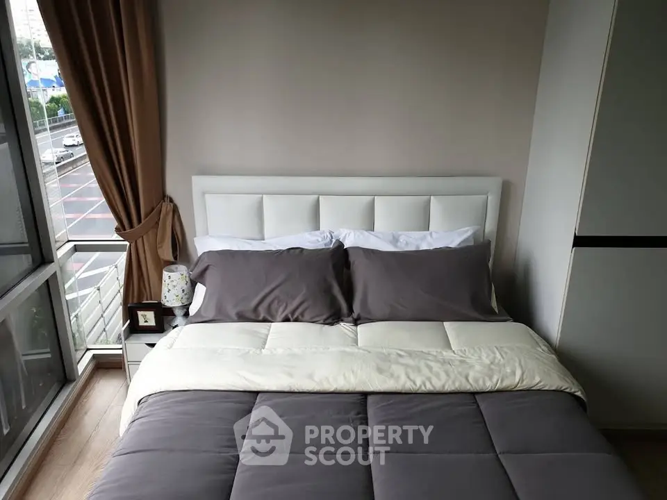 Cozy bedroom with modern decor and large window offering city views.