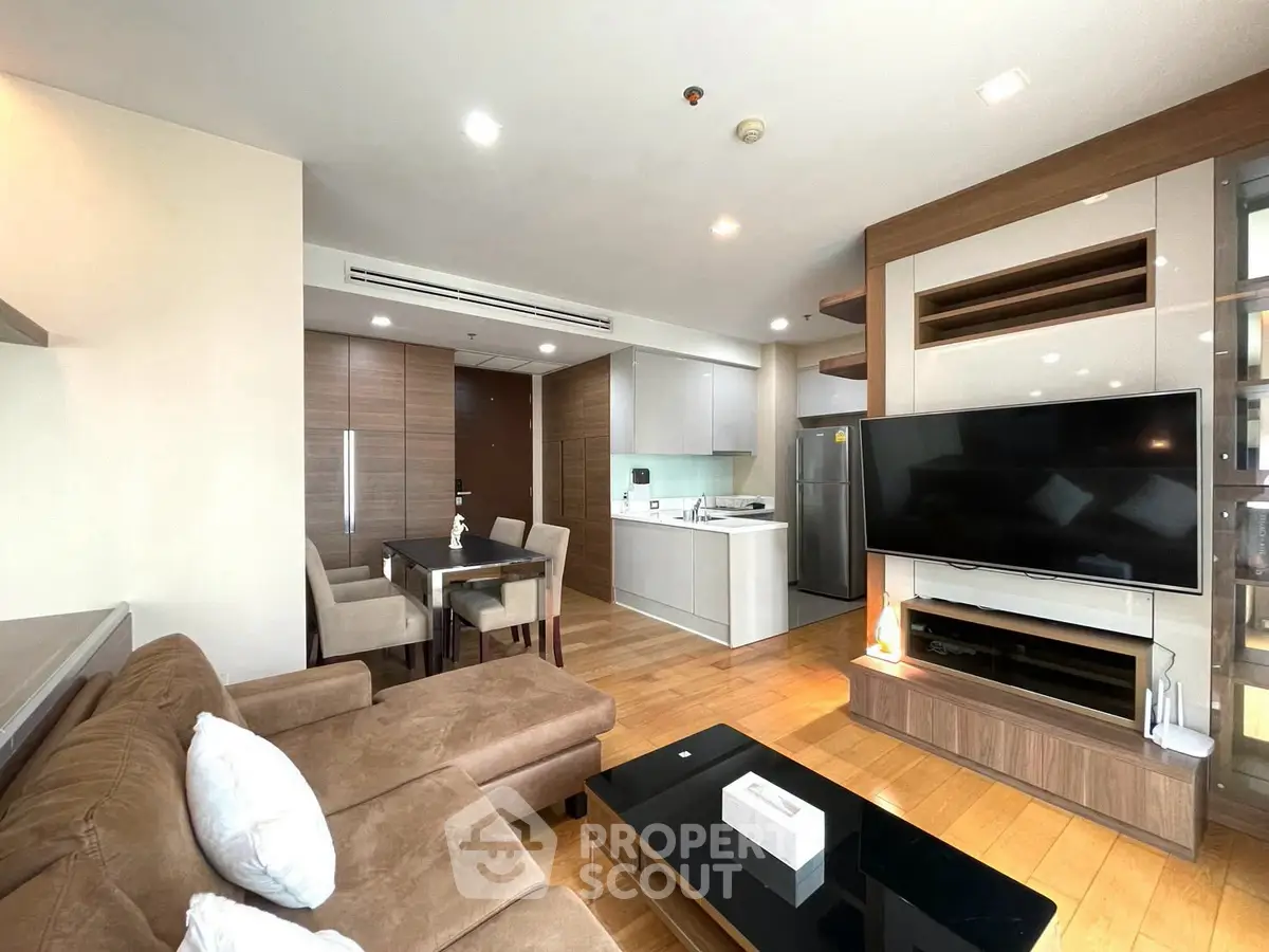 Spacious modern living room with open kitchen and dining area, featuring a large TV and cozy seating.