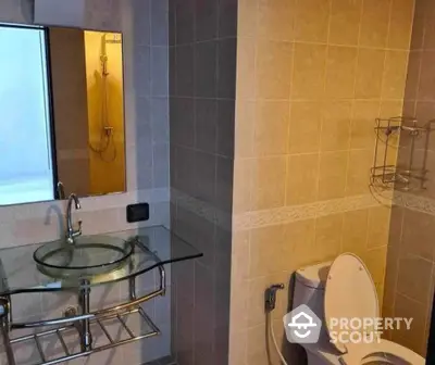 Cozy bathroom with modern glass sink and mirrored shower, featuring neutral tilework and well-placed lighting for a serene ambiance.