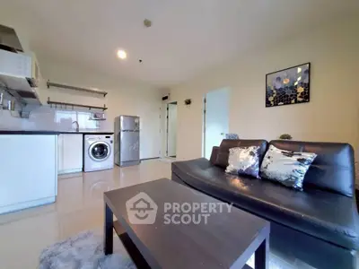 Modern living room with sleek black sofa, washing machine, and stainless steel fridge in open layout.
