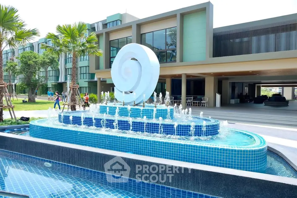 Luxurious modern building with stunning pool and artistic fountain in a lush green setting.