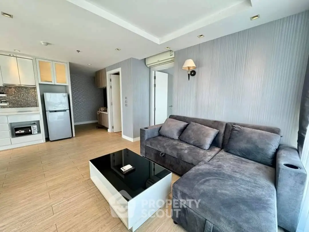 Modern living room with stylish gray sofa and sleek kitchen area in open layout apartment.