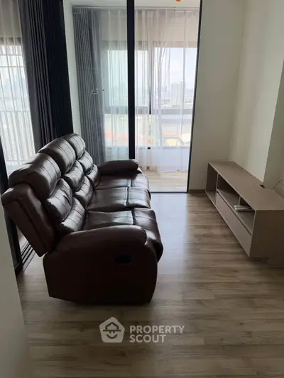 Modern living room with leather sofa and balcony view in high-rise apartment.