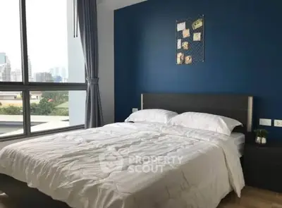 Modern bedroom with large window and city view, featuring a cozy bed and stylish decor.